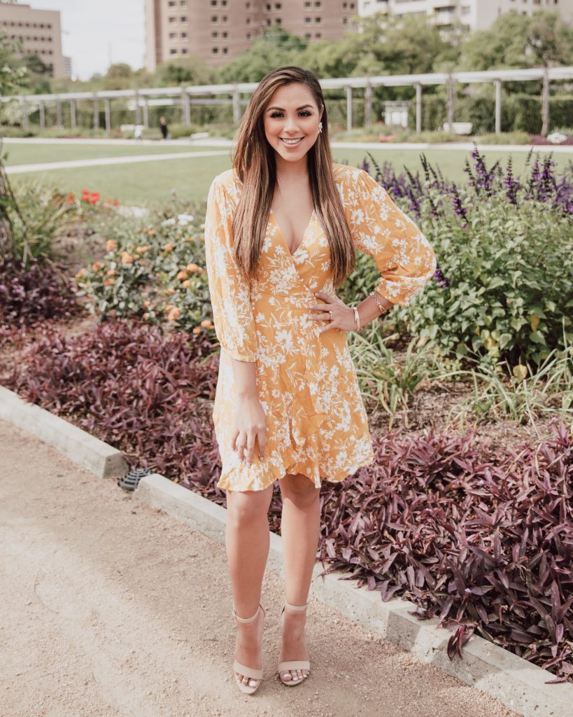 Blogger is wearing a mustard yellow floral wrap dress. The dress length is above the knee. The bottom hem is ruffled and 3/4 sleeves cover the shoulders. Great dress for a casual Easter. See more at thefashionablemaven.com