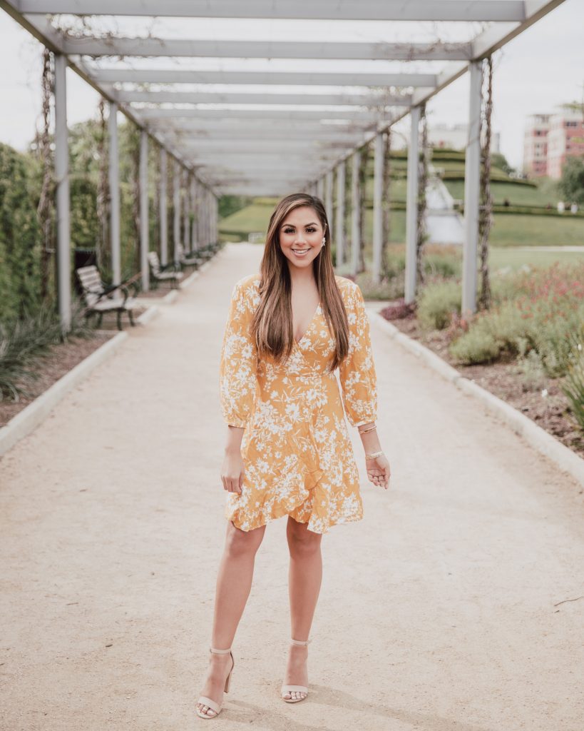 Casual look. Blogger is wearing a mustard yellow floral wrap dress. The dress length is above the knee. The bottom hem is ruffled and 3/4 sleeves cover the shoulders. Great dress for a casual Easter. See more at thefashionablemaven.com