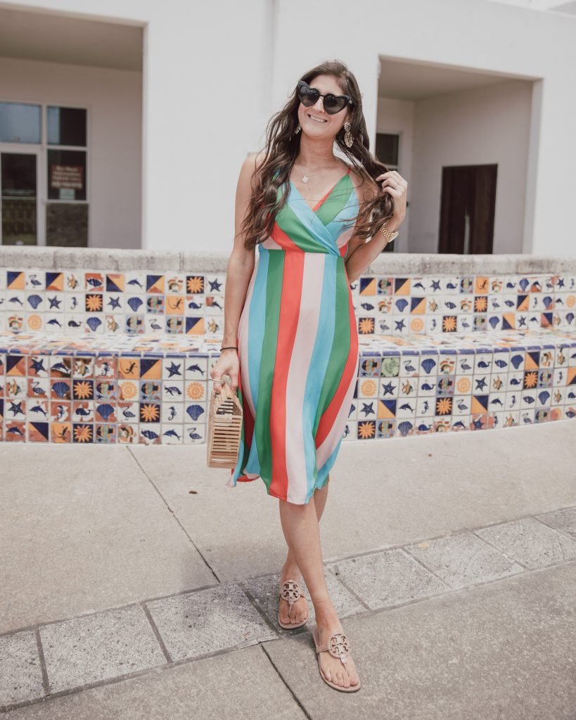 Jenni Metz- The Fashionable Maven is wearing a colorful striped dress, denim jacket, Tory Burch sandals, heart sunglasses, and bamboo bag. Click to see more striped dress outfits. #summer #stripes #spring