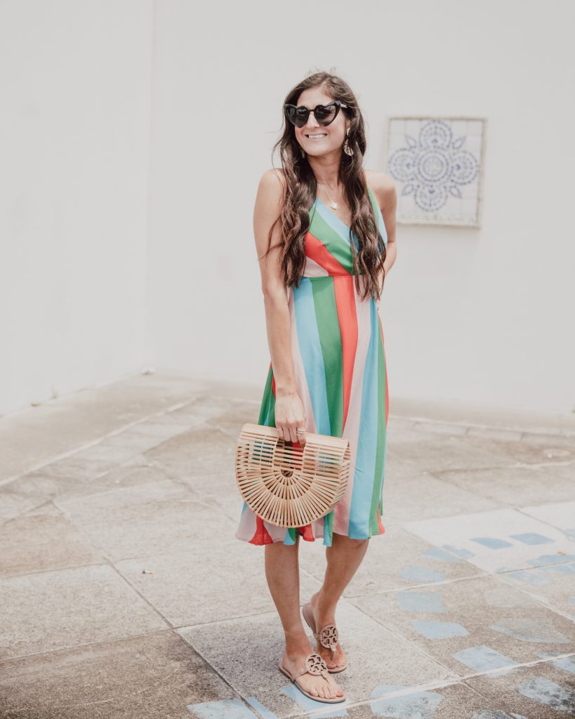 Jenni Metz- The Fashionable Maven is wearing a colorful striped one piece dress, denim jacket, Tory Burch sandals, heart sunglasses, and bamboo bag. Summer stripes. Click to see more striped dress outfits. #summerfashion #stripes #onepiece